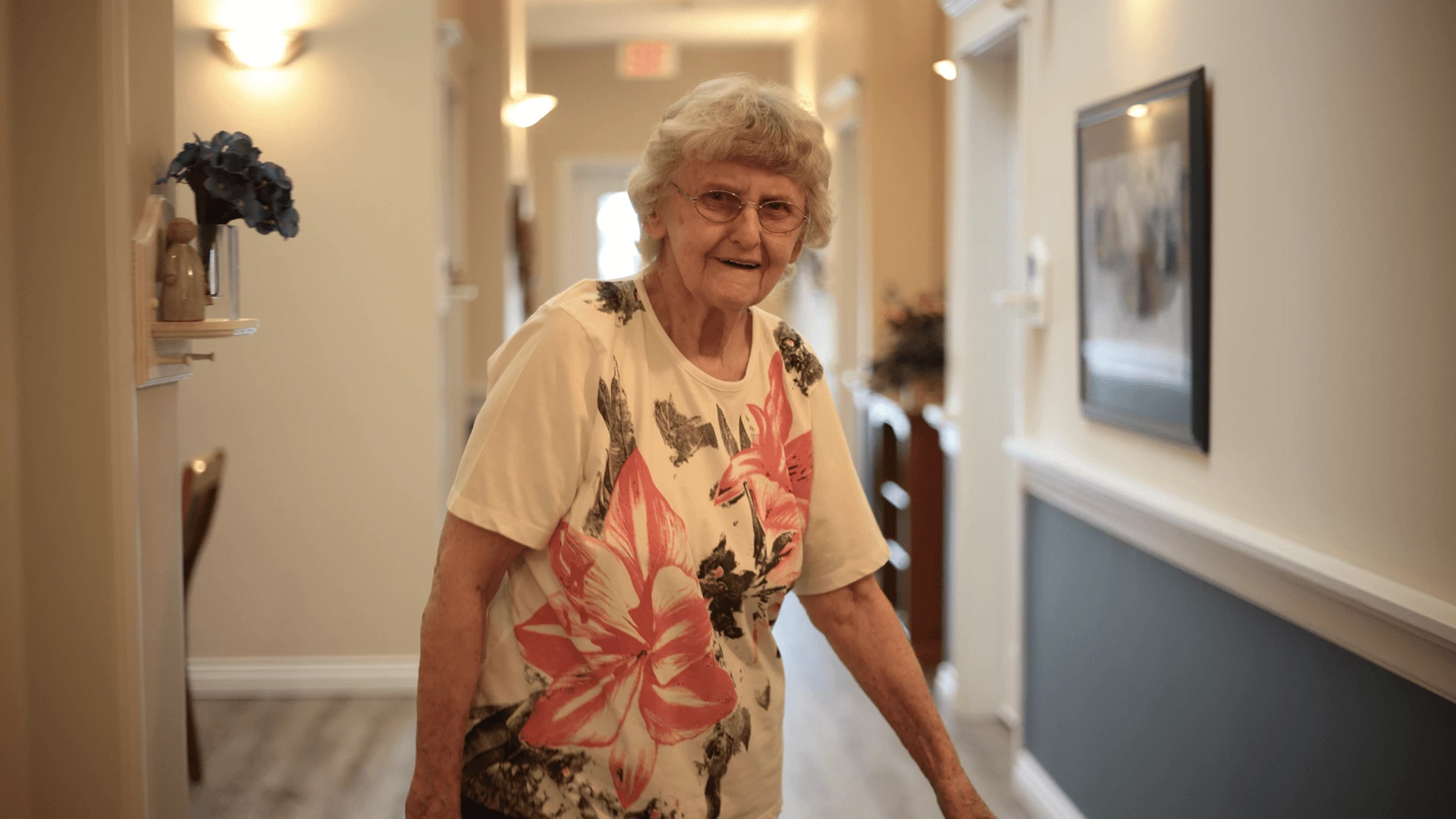 Senior woman standing in hallway, smiling at the camera